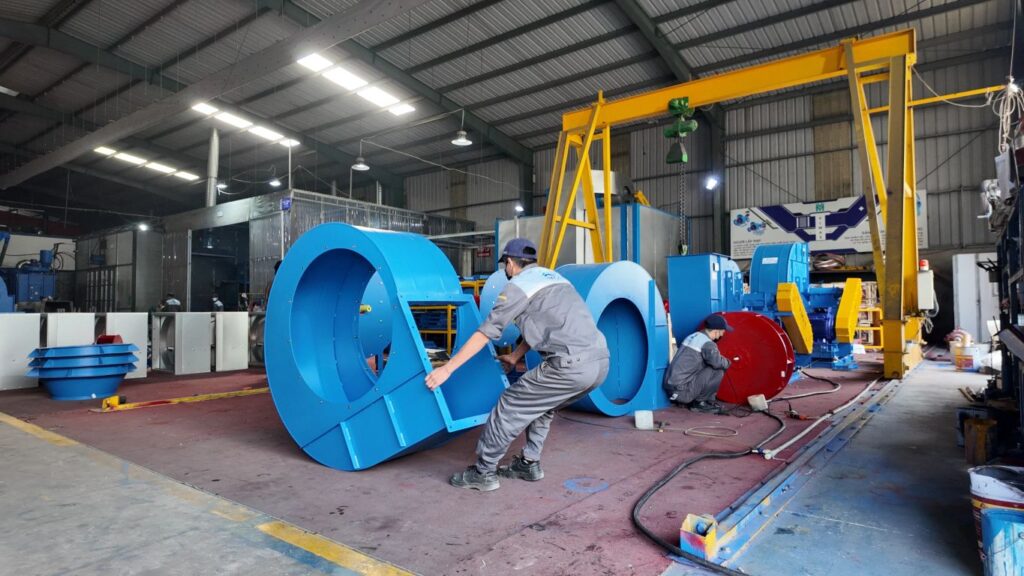 Workers assembling large blue industrial components in a factory.